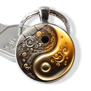 Close-up of artistic yin-yang glass dome keychain with gold and black fluid art design