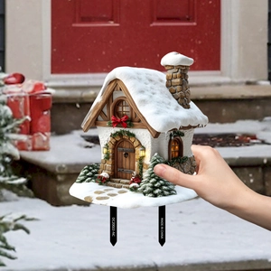 Detailed view of a miniature Christmas snow cottage garden stake with festive red bow