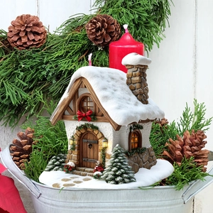Close-up of a festive miniature Christmas snow cottage nestled in a decorative pine display