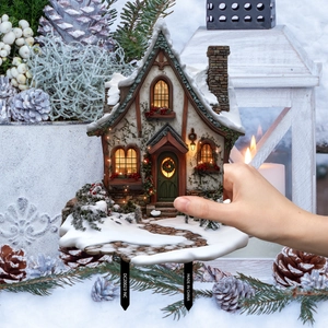 Close-up of a snowy Christmas garden cottage stake with warm lights and dual ground pins