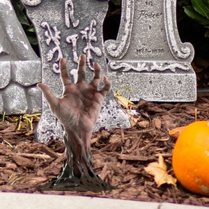 Close-up of realistic zombie hand stake rising from soil for Halloween garden decor