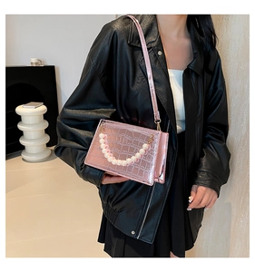 Detail of pink metallic crocodile pattern bag with pearl strap worn by a model