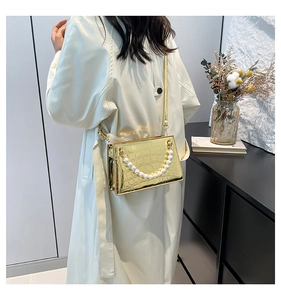 Close-up of golden faux crocodile skin texture and elegant pearl handle on square bag