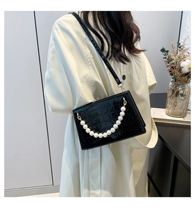 Detail of black faux leather crossbody bag with crocodile texture and pearl chain
