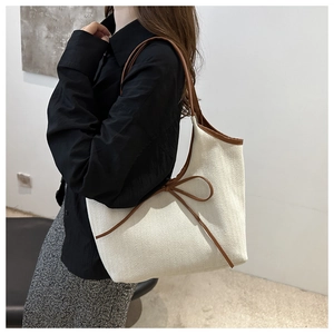 Detail of canvas tote bag featuring brown leather trim and large bow decoration