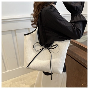Detailed texture of beige linen tote bag featuring black trim and bow handle detail