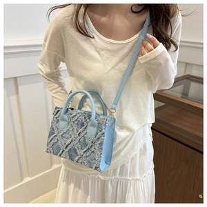 Close-up of light blue denim mini square bag with frayed fringe texture on model