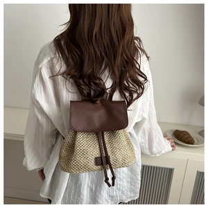 Detail of a straw and brown leather backpack with drawstring closure shown on a model