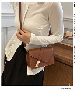Detail of a brown leather crossbody bag with a golden metal buckle on a minimalist flap
