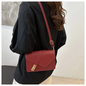 Close-up of red leather flap bag with detailed gold metal twist lock and adjustable strap