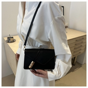 Detail of minimalist black crossbody bag with gold twist lock on a minimalist wood dresser