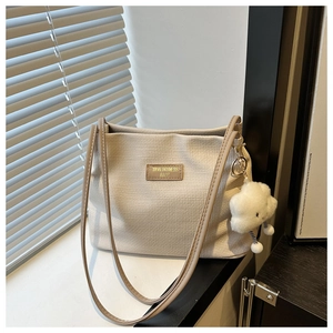 Detail of beige waffle textured tote bag featuring a cloud plush pendant and dual straps