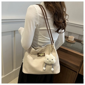 Detail of beige woven tote bag with brown leather straps and cloud plush charm