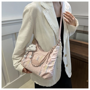 Vue détaillée du sac hobo rose gaufré avec un pendentif en peluche nuage souriant