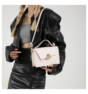 Detailed view of cream leather crossbody bag with gold buckle on a black leather outfit