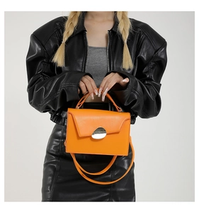 Detailed close-up of a vibrant orange leather handbag with silver metallic buckle on a model