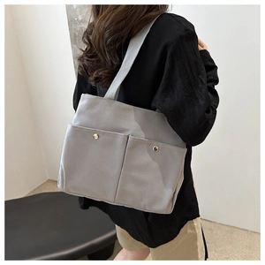 Close-up of gray canvas tote bag featuring dual front pockets with silver snap buttons