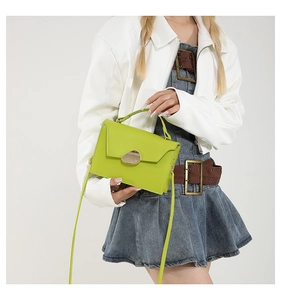 Model wearing a bright neon green crossbody bag with gold buckle and smooth leather finish
