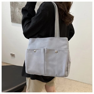 Side view of a light gray canvas tote bag with front pockets on a model for daily commute