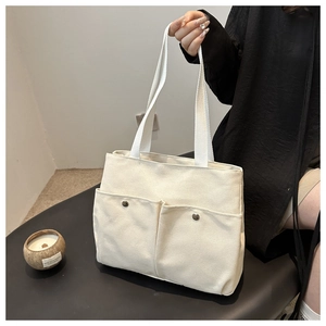 Detail of minimalist canvas tote bag showing large front pockets and durable woven handle