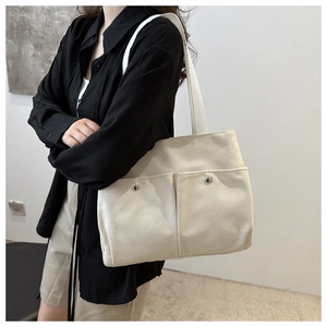 Detailed view of beige canvas tote bag with front pockets and silver metal buttons