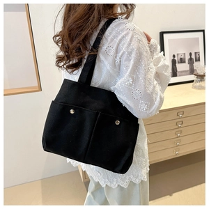 Black canvas tote bag with dual front pockets shown on model in minimalist interior