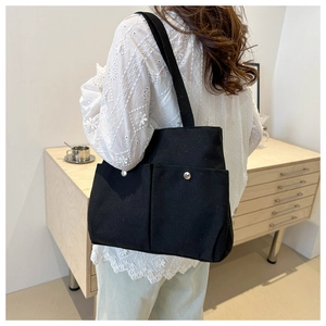 Detail of black canvas tote bag showing double front pockets and silver snap buttons