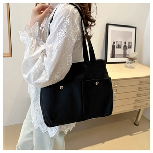 Close-up of black canvas tote bag showing two front pockets with silver metal buckles