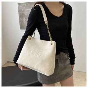 Détail du sac cabas crème avec texte embossé et bandoulière en chaîne dorée
