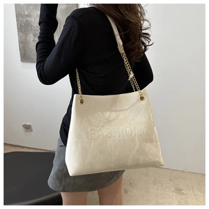 Close-up of beige tote bag with gold chain strap and embossed fashion lettering details