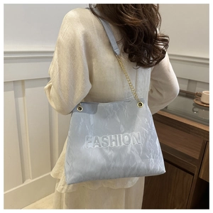 Detail of light blue wrinkled tote bag with gold chain strap and FASHION lettering