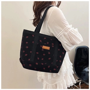 Detail of strawberry pattern corduroy tote bag with leather logo patch on black fabric