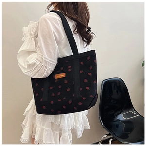 Detailed view of black corduroy tote bag with red strawberry embroidery and brown logo patch