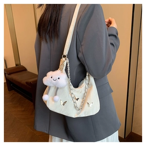 Detail of a beige crescent bag featuring silver butterfly motifs and a plush cloud charm