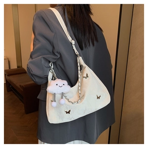 Detail of cream crescent shoulder bag featuring metal butterfly and cloud charm