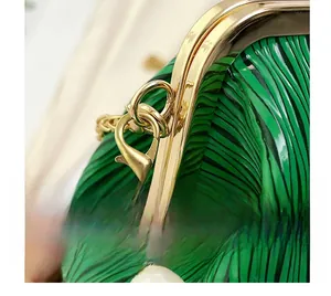 Detail of the golden metal buckle and chain connection on a green pleated evening clutch bag