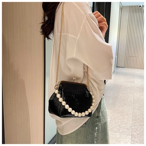 Detail of pleated black shell bag with pearl handle and golden chain strap on model