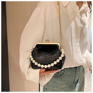 Detail of black pleated mini clutch bag with pearl handle and golden chain on model