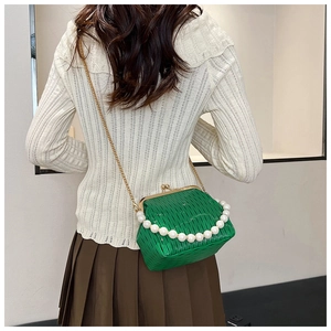 Detail of green pleated crossbody bag featuring pearl handle and golden chain strap
