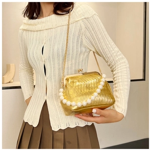 Detailed view of golden pleated clutch with pearl handle and metallic chain strap