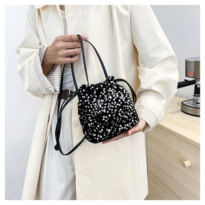 Détail du sac seau noir à paillettes avec cordon porté sur un trench-coat beige