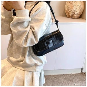Detail of glossy black crocodile pattern leather shoulder bag with flip buckle closure