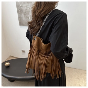 Detailed view of a brown suede fringed shoulder bag with a silver chain strap on model