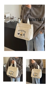 Detail view of a beige canvas tote bag with cartoon bear illustrations and front pocket