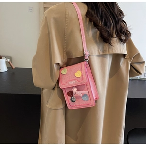 Detail of pink vintage crossbody bag with heart patches, ribbon bow, and FASHION logo