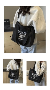 Detail of black canvas tote bag showing wide shoulder strap and bold white graphic print