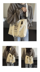 Detail of white canvas tote bag showing reinforced leather accents and bold typography print