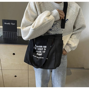 Detail view of large black canvas tote bag with white artistic letters and adjustable strap