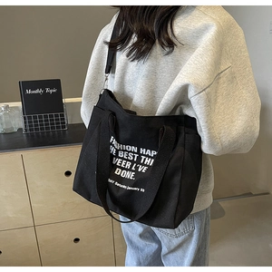 Side view of a large black canvas tote bag with white lettering on a female model