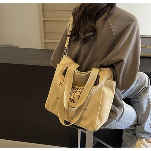 Detail of a large beige canvas tote bag with wide double handles and shoulder strap